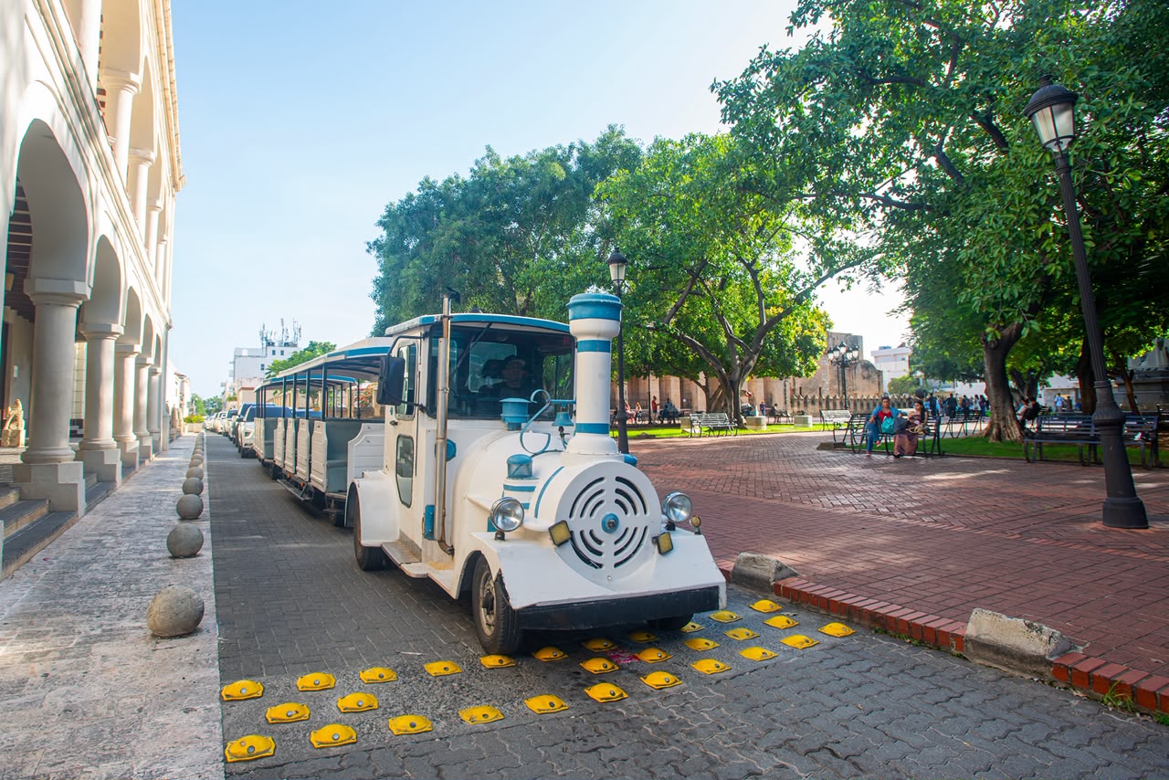 Tren turístico junto a una torre con cúpula y palmeras